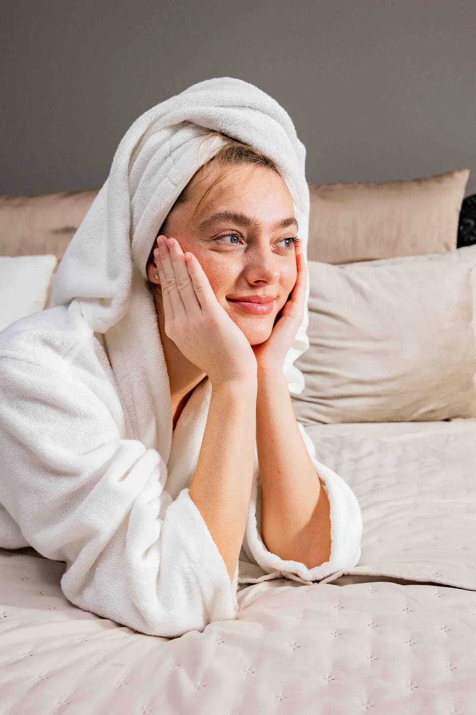 Woman wrapped in a white towel resting her face on her hands, Avora Beauty
