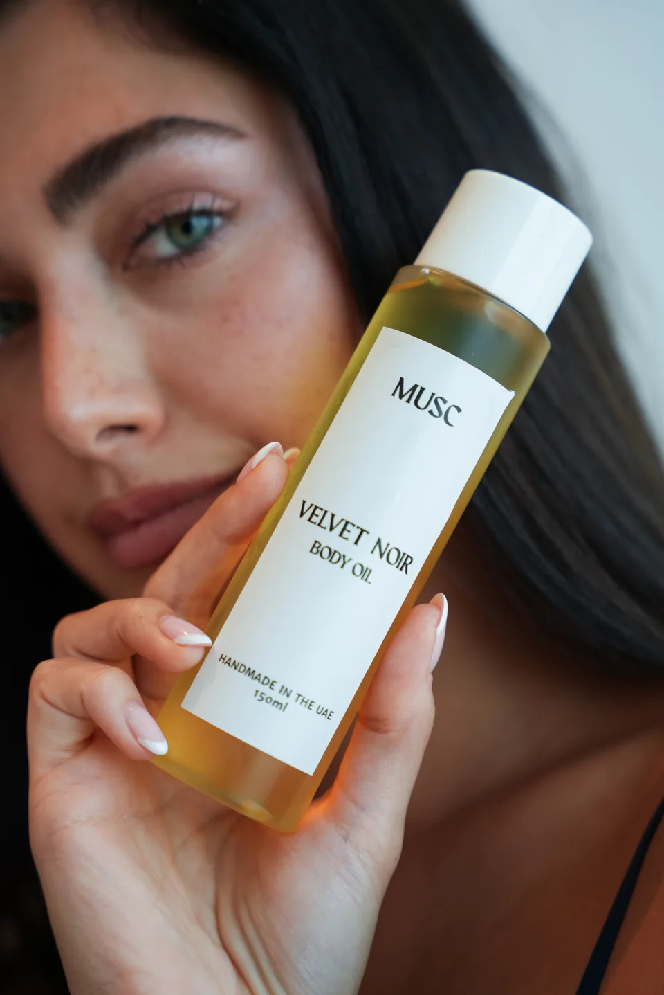 Woman holding a MUSC Velvet Noir body oil bottle