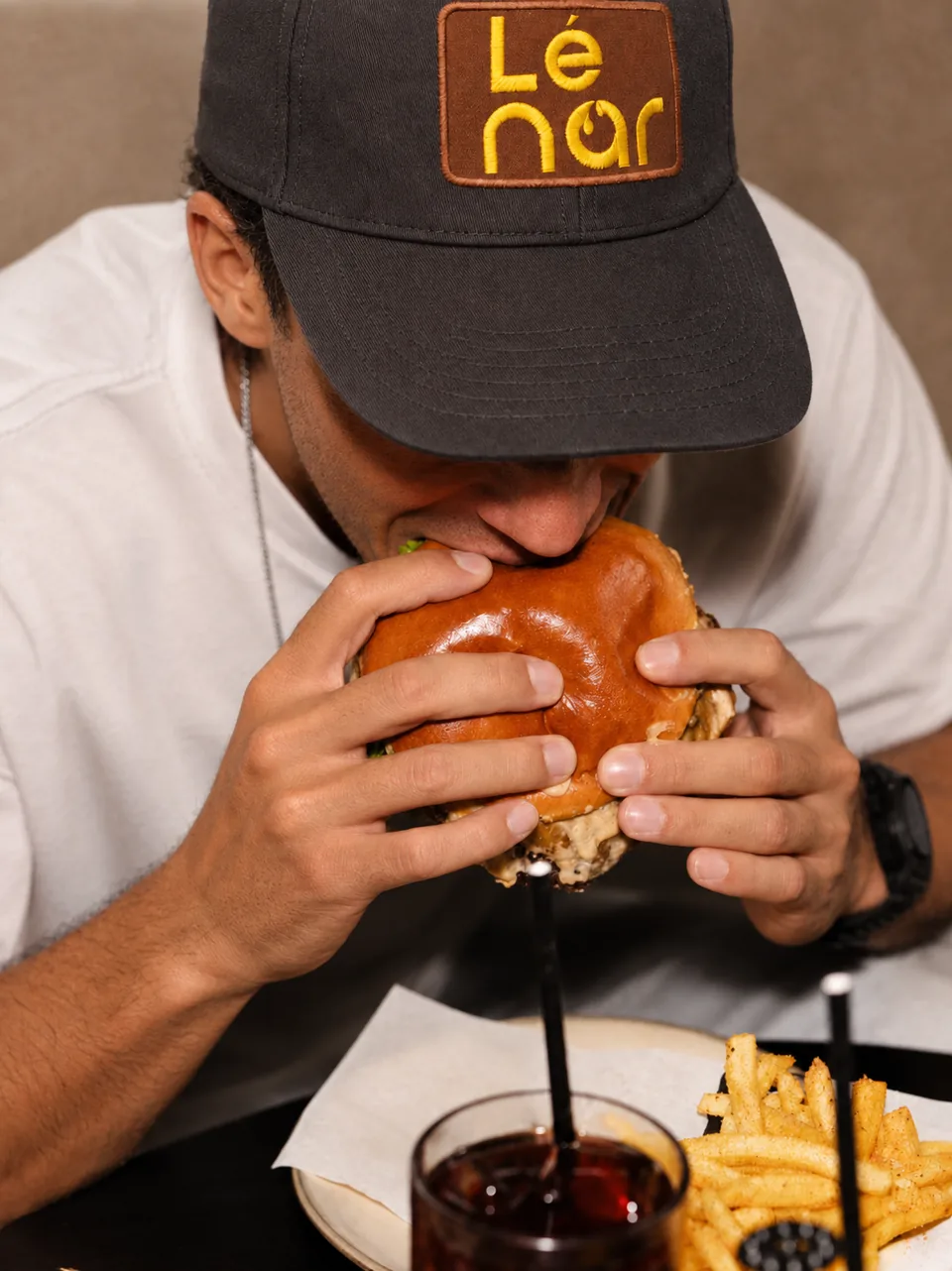 Man in a Lenar cap about to bite into a smash burger
