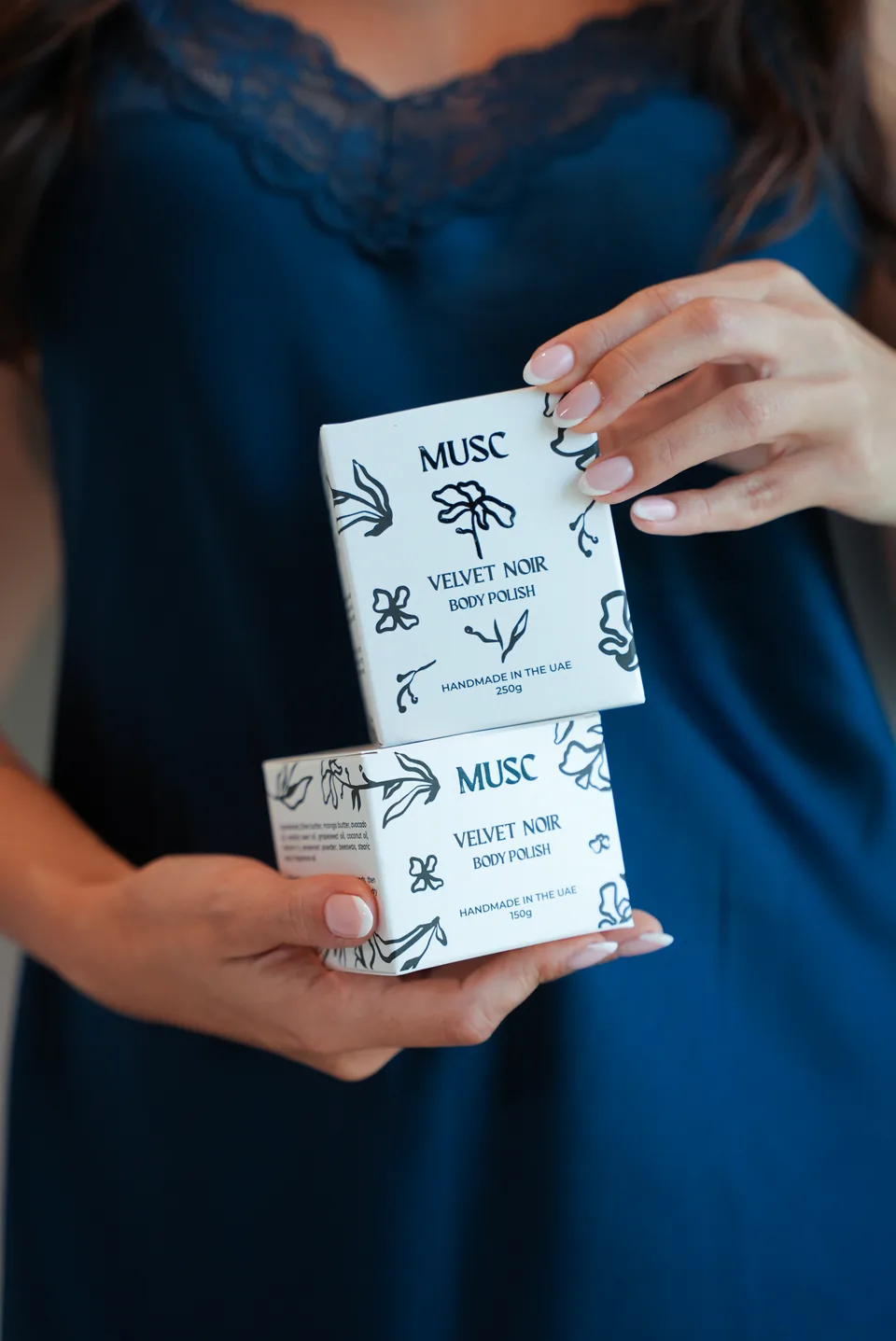 Hands holding Musc Velvet Noir body polish and body oil boxes